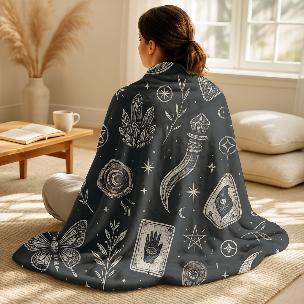 Person sitting on a couch wearing a dark blanket with white symbols and designs.