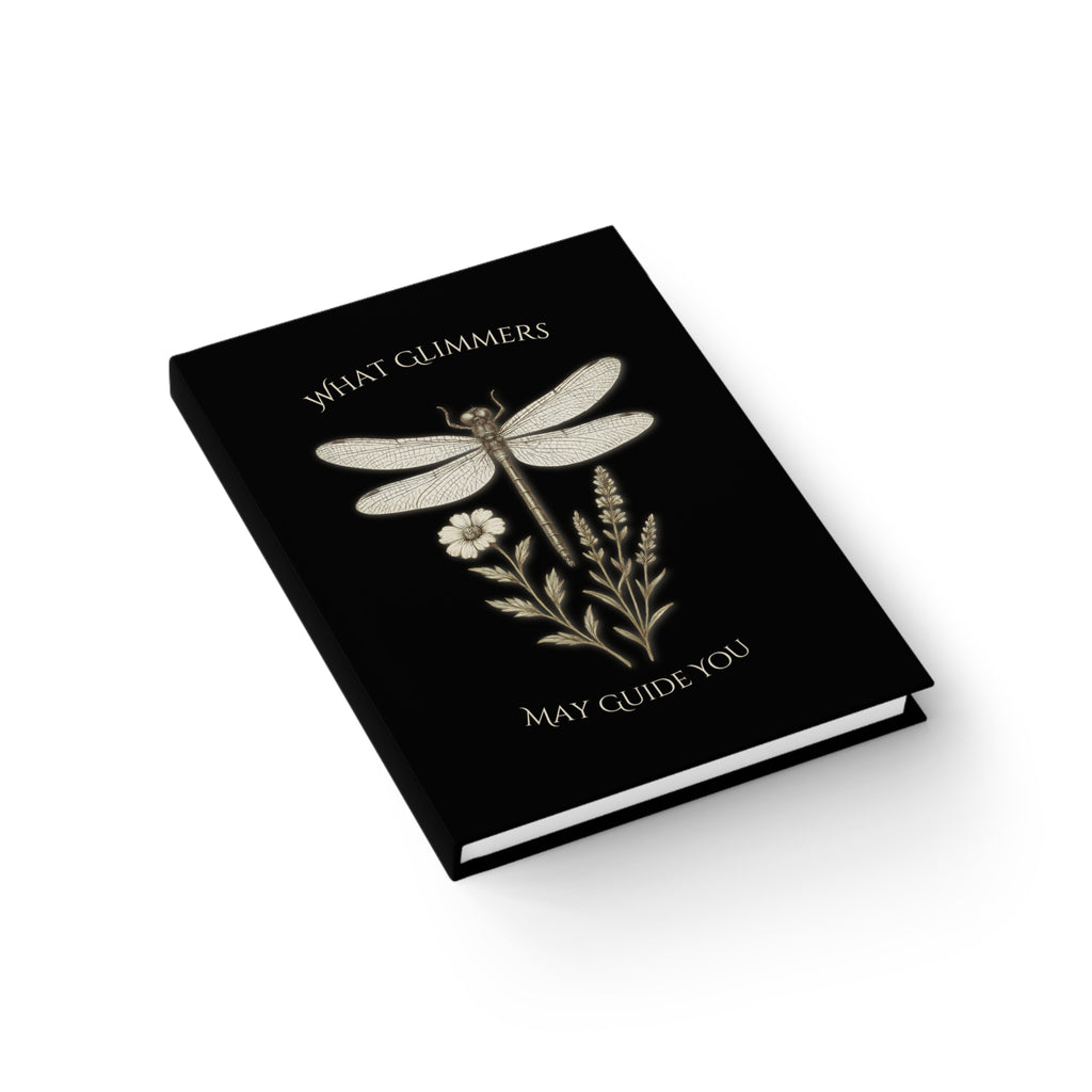 Black book with dragonfly illustration and text on a white background. "What Glimmers May Guide You" Dragonfly Journal